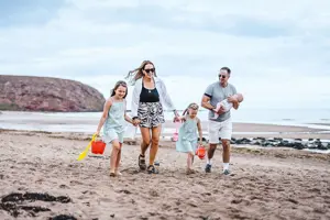 Family walking along the beach at Pease Bay with buckets and spades 