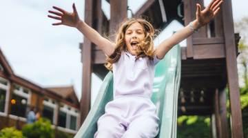Young girl smiling and playing on a slide in a playground 