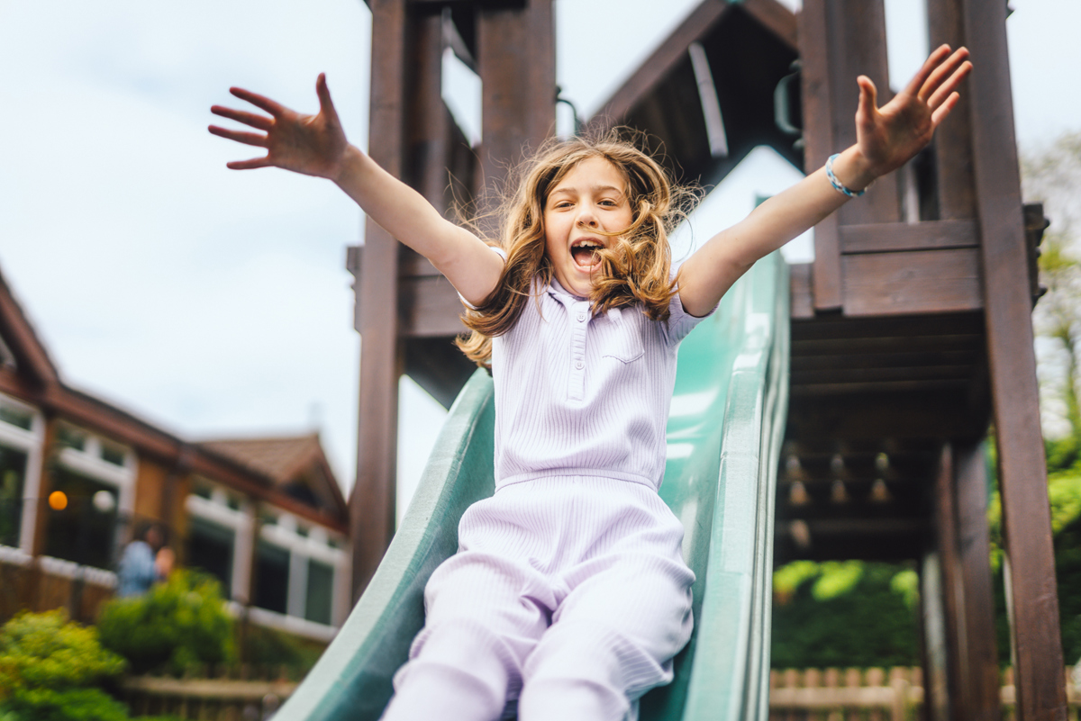 Young girl smiling and playing on a slide in a playground 