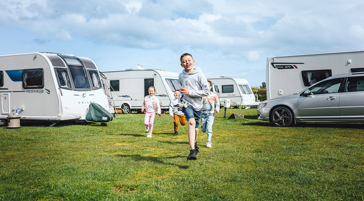 Four children running together on a green grassy field next to touring vans and motorhomes on their pitches 
