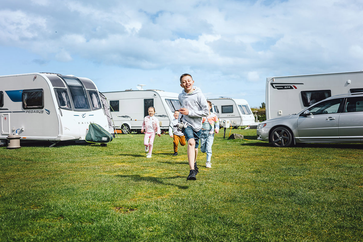 Four children running together on a green grassy field next to touring vans and motorhomes on their pitches 