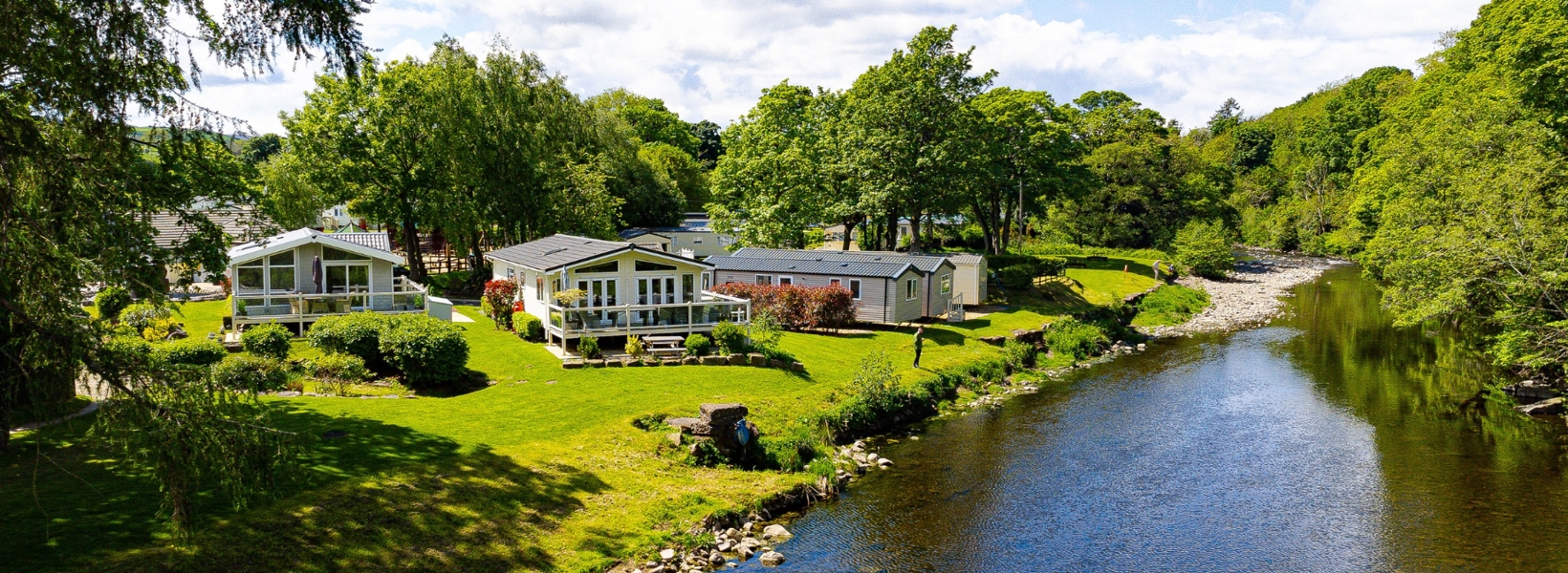 Caravans and lodges holiday homes at Kingfisher Leisure Park in County Durham with trees and a river next to them