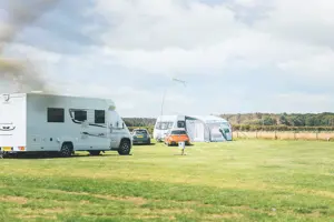Two touring vans and cars parked on touring pitches at a UK holiday park with green grass and a blue sky above 