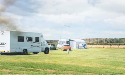 Two touring vans and cars parked on touring pitches at a UK holiday park with green grass and a blue sky above 