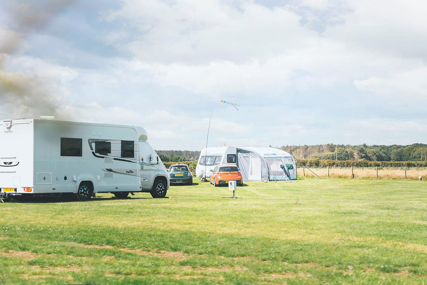 Two touring vans and cars parked on touring pitches at a UK holiday park with green grass and a blue sky above 