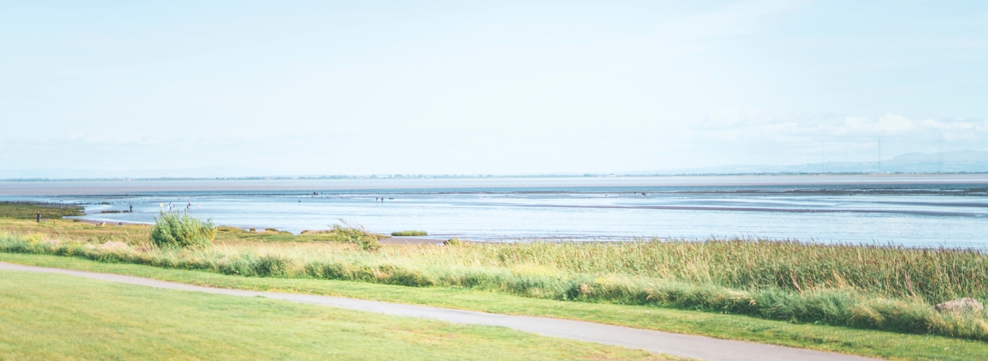 The sea at Powfoot Beach against a blue sky with grass and a footpath in front at Queensberry Bay